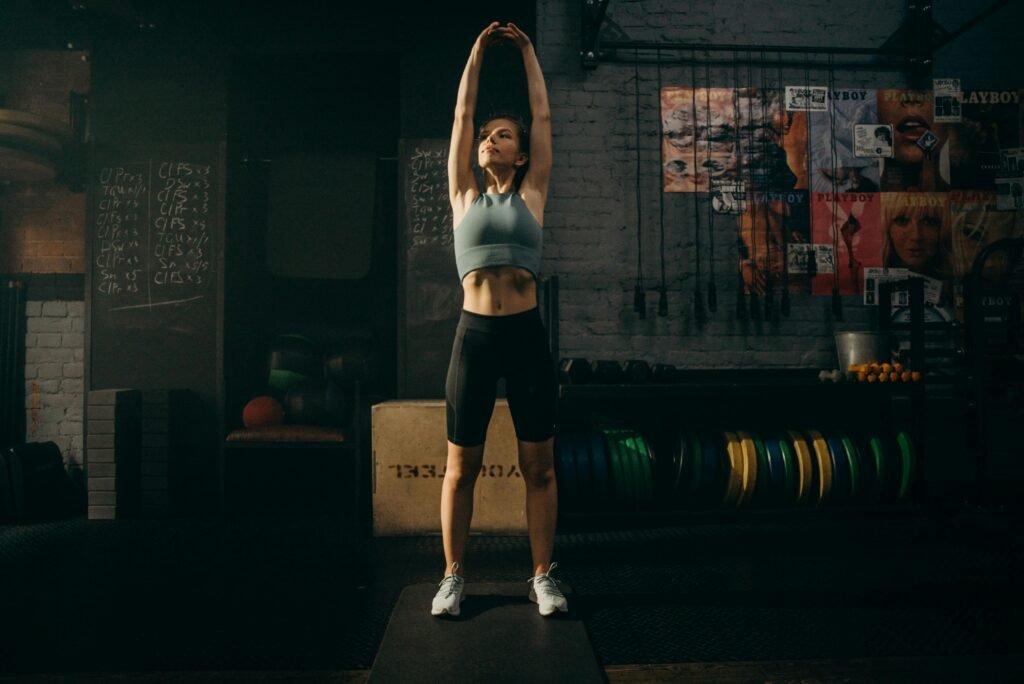 pexels-photo-4753892-4753892 Strong woman stretching her arms in an industrial-style gym environment with motivational wall art.